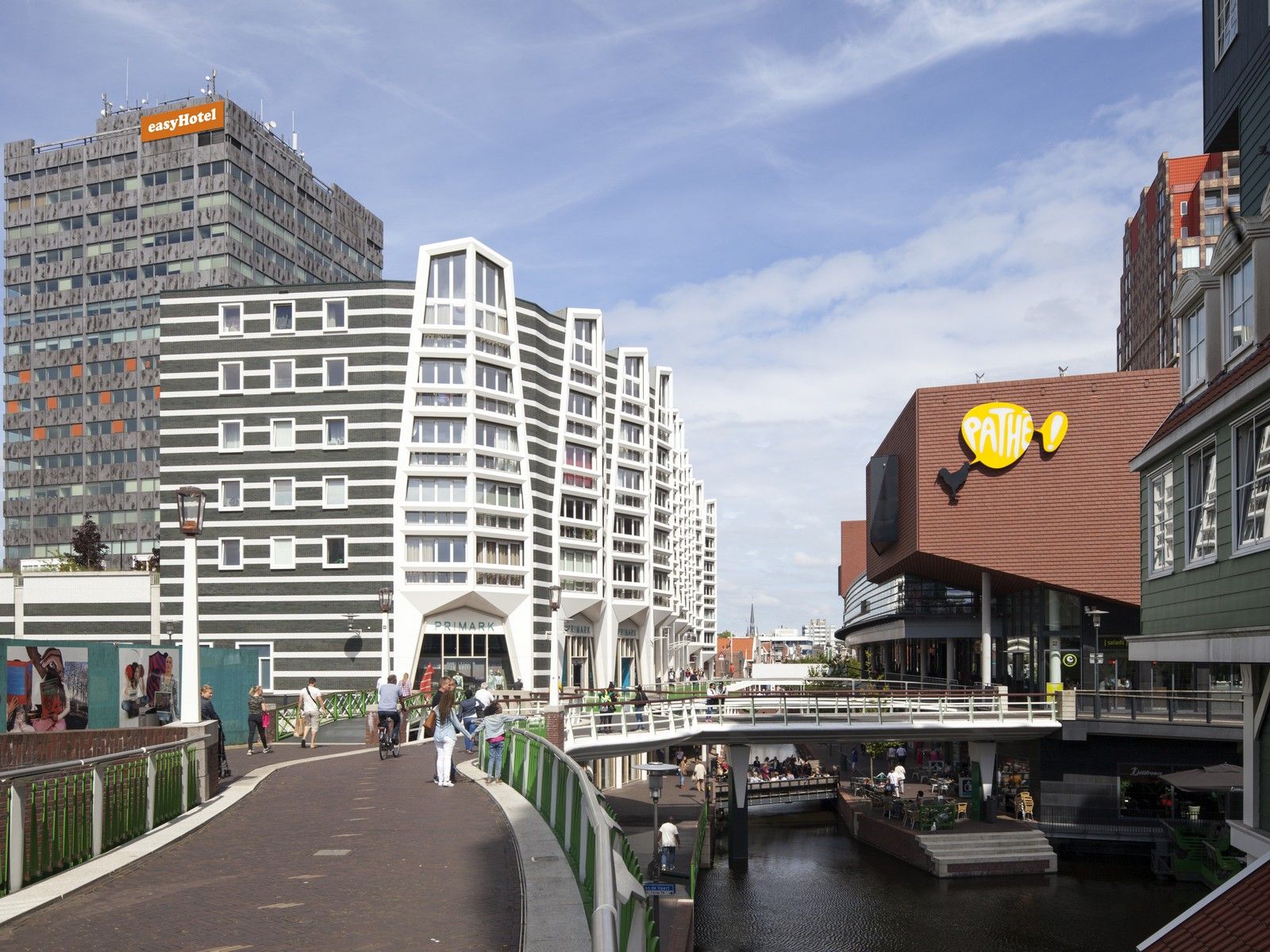 Modern architecture in Zaandam city center, Netherlands, featuring the easyHotel building, a Primark store, and a Pathé cinema, alongside a canal with bridges and pedestrians.