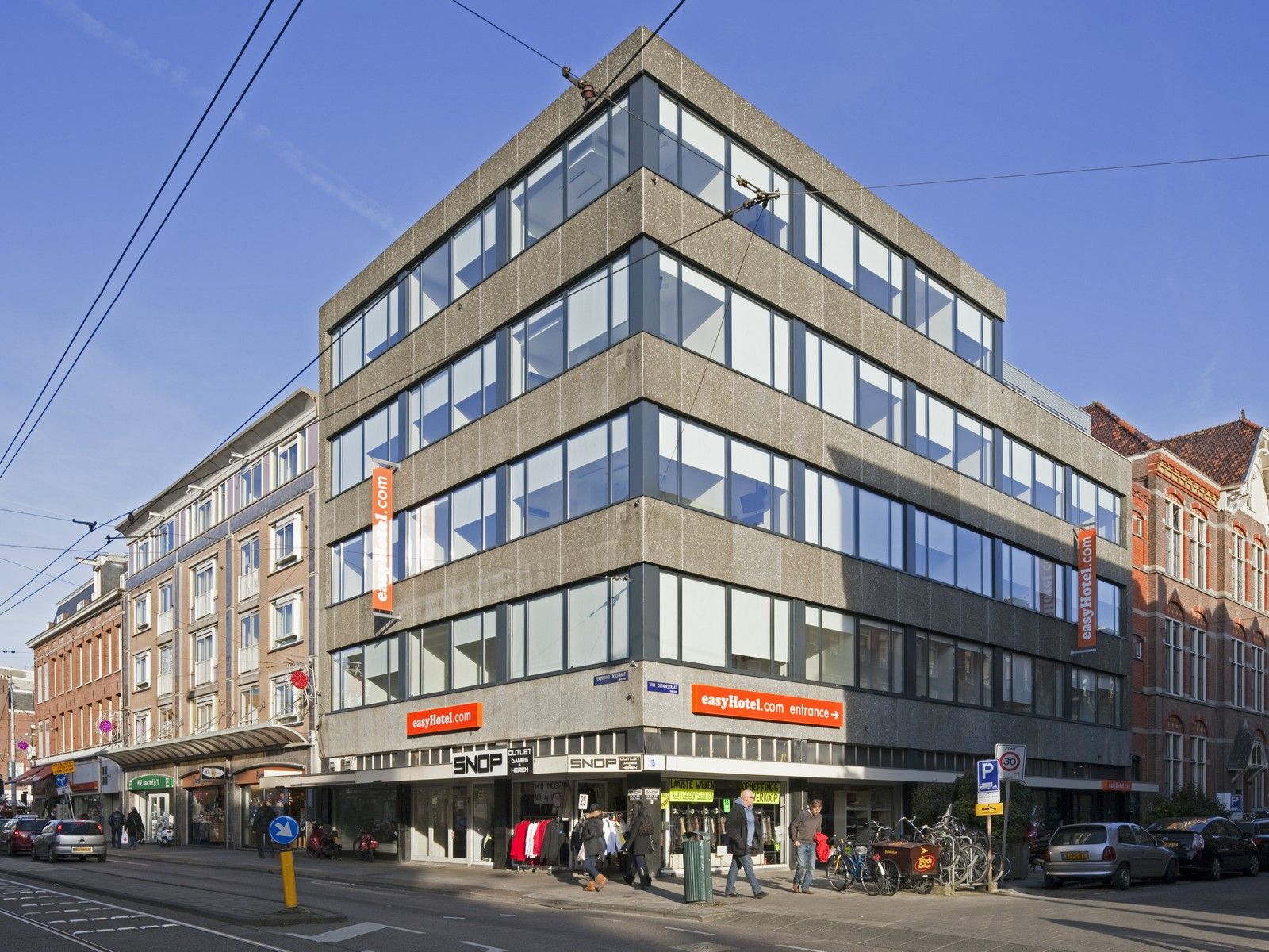 Exterior view of the modern easyHotel building in Amsterdam, featuring a concrete facade and large windows, situated on a busy city street with pedestrians and bicycles.
