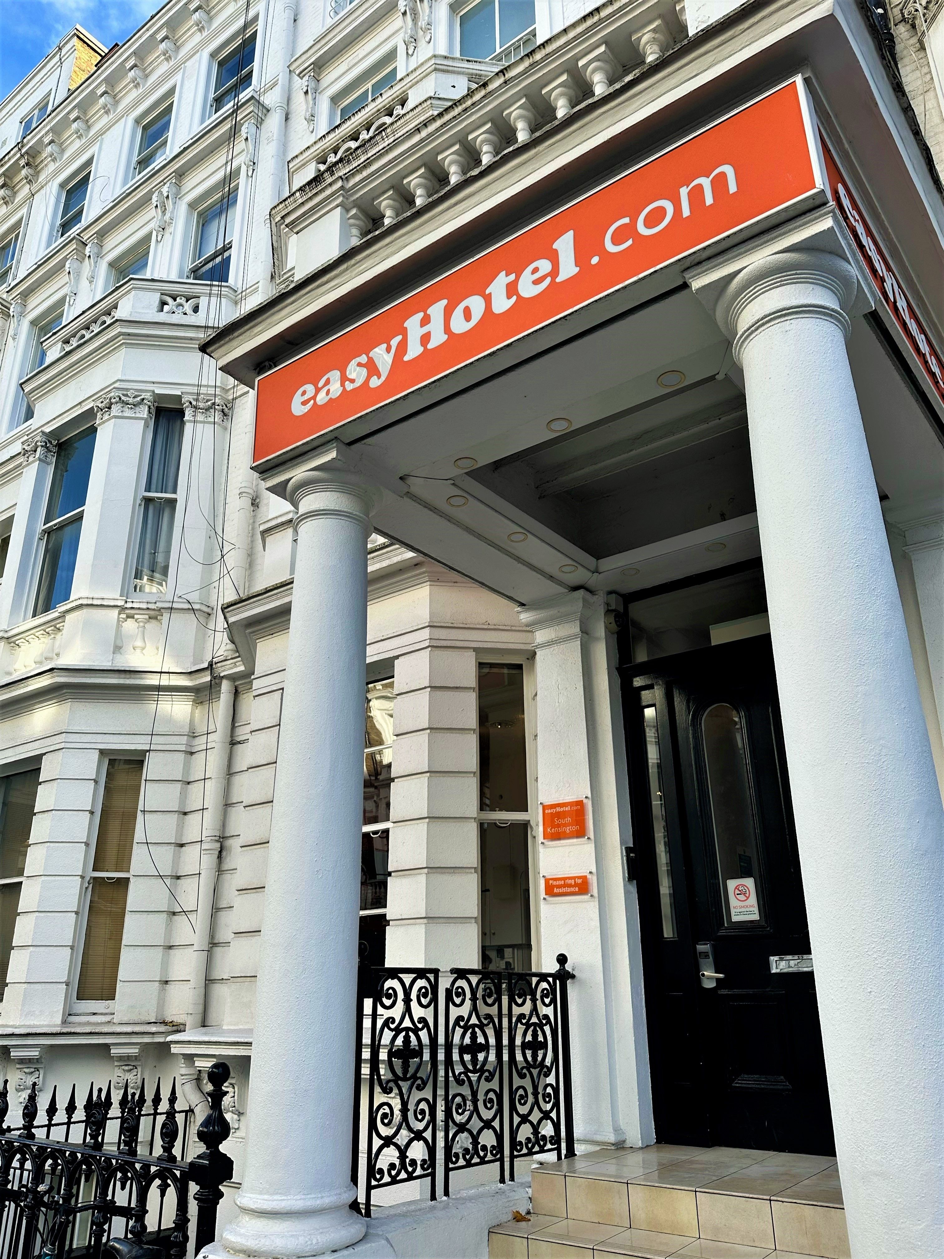 Exterior view of the easyHotel in South Kensington, London, a white stucco building with an orange "easyHotel.com" sign above its entrance.
