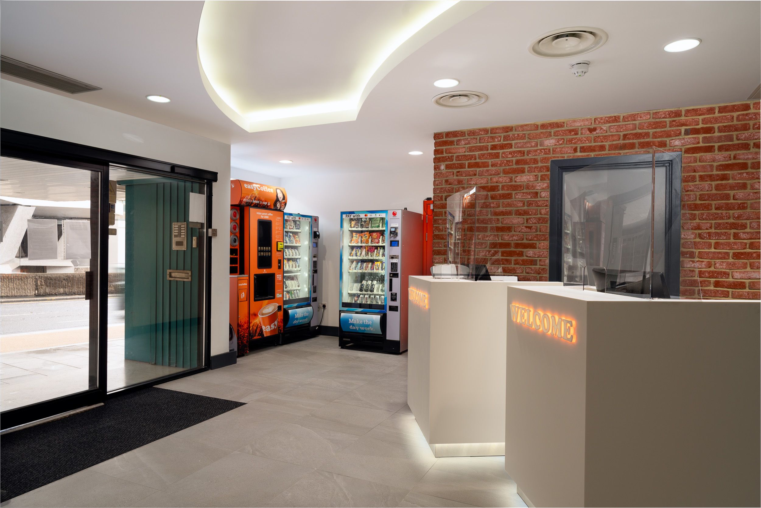 Modern easyHotel reception lobby featuring white self-check-in desks, easyCoffee and snack vending machines, and automatic glass entrance doors.