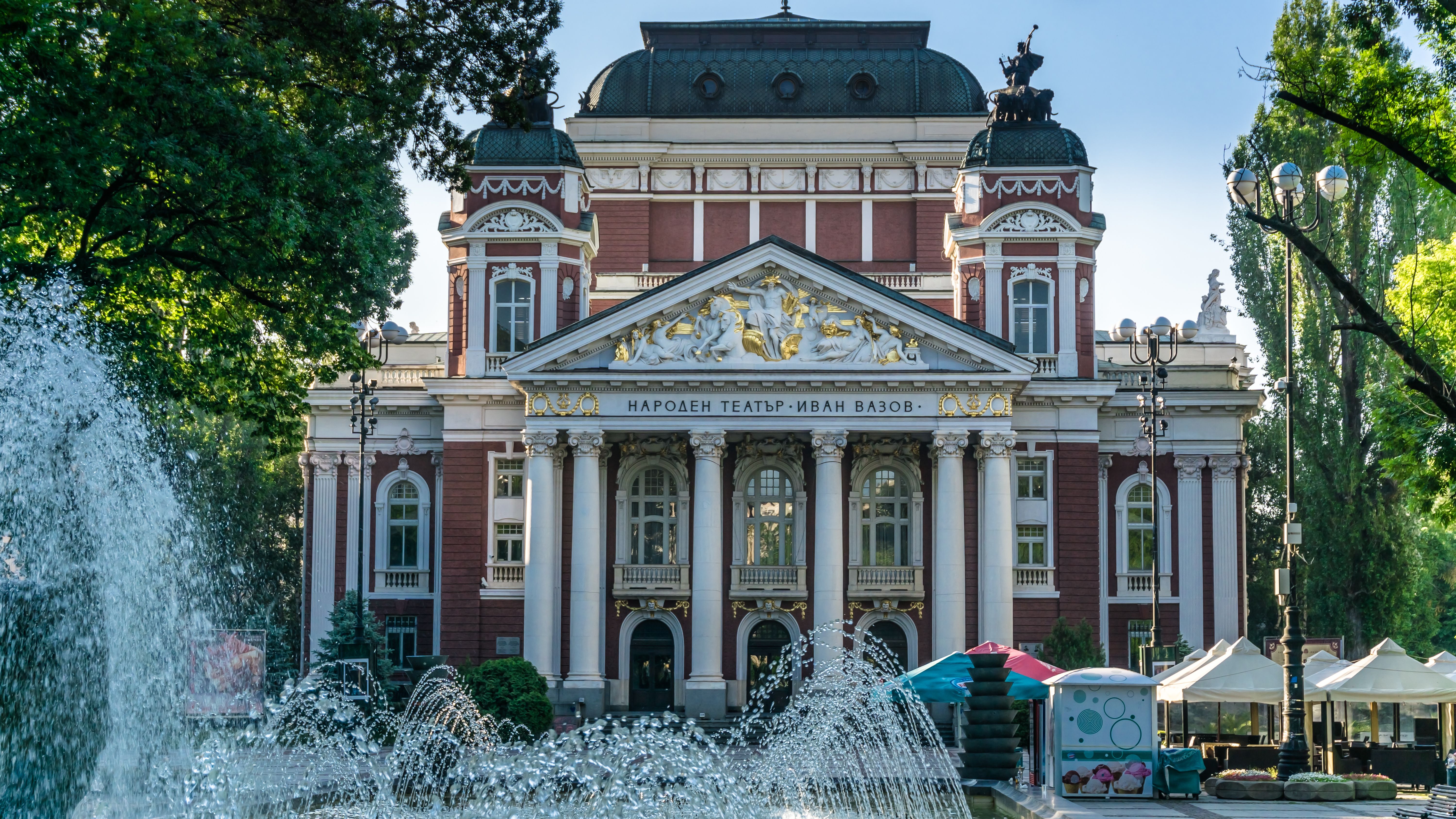 Ivan Vazov National Theatre in Sofia, Bulgaria, a grand neoclassical building with a red and white facade, columns, and a prominent fountain in the foreground.