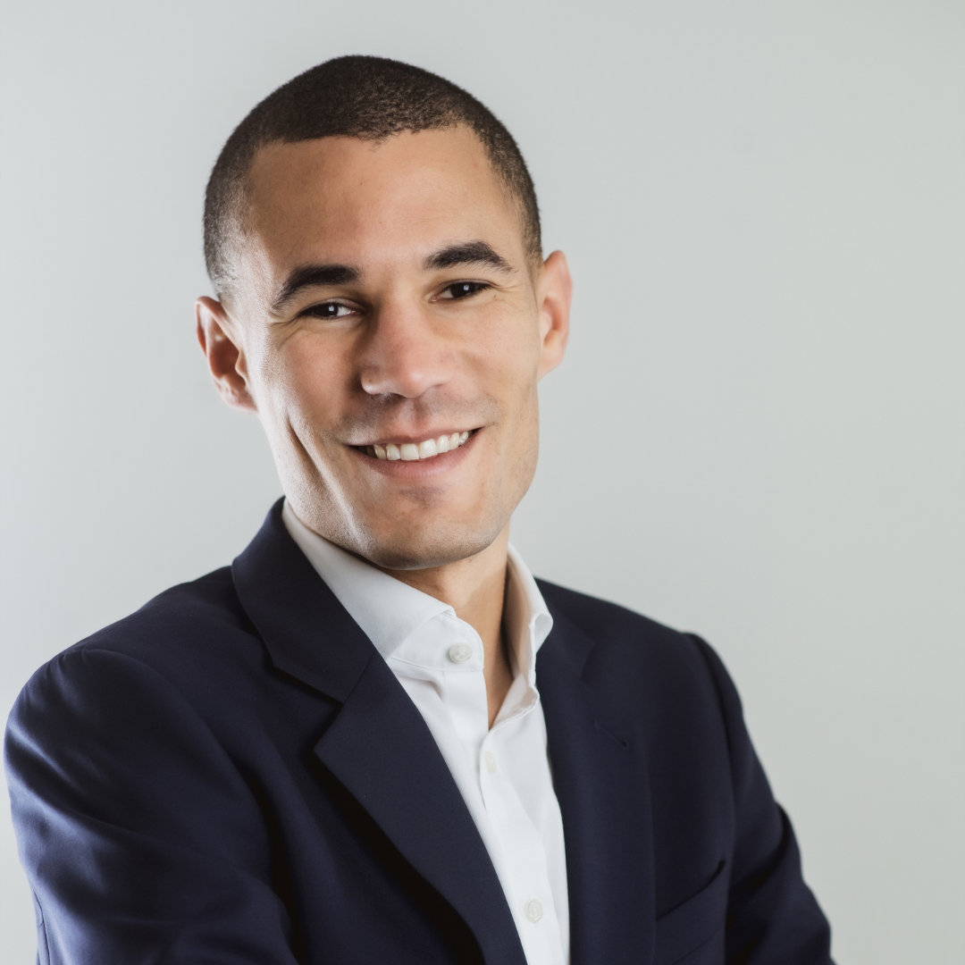 Professional portrait of a smiling man in a dark suit and white shirt against a plain background.