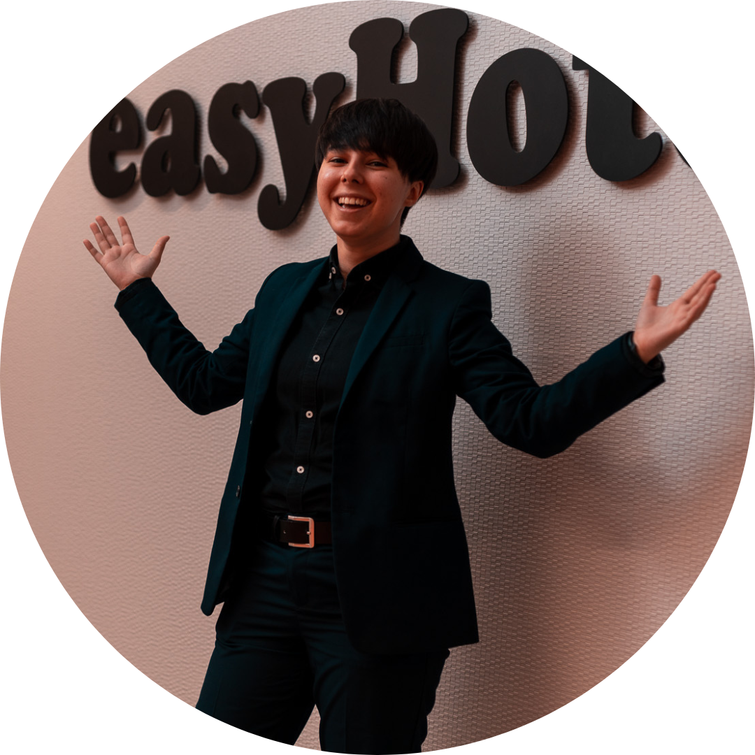 Smiling person in a dark suit with arms outstretched, welcoming guests in front of a wall with the easyHotel logo.