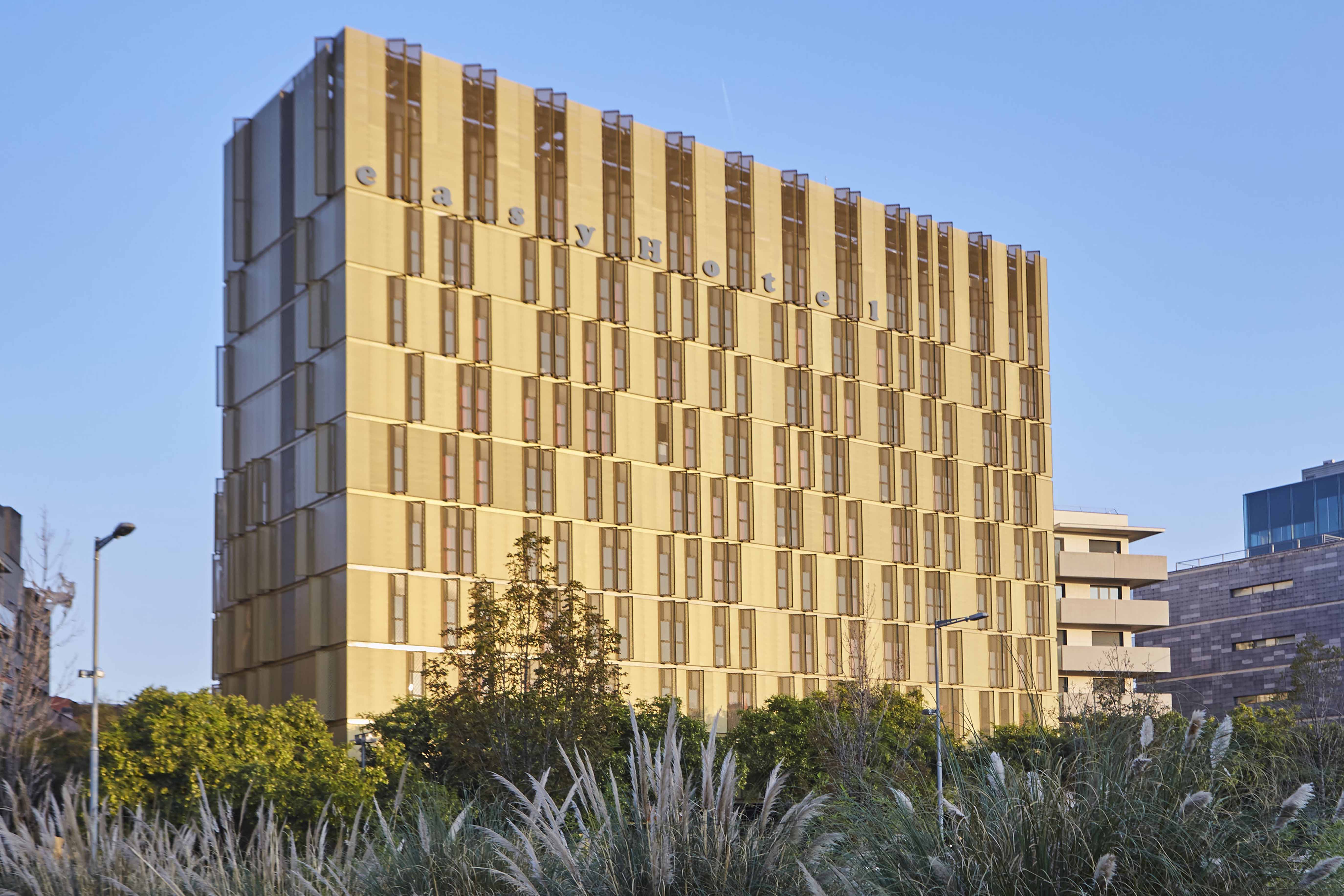 easyHotel Barcelona Fira building exterior, a modern high-rise hotel with numerous small windows, under a clear blue sky.