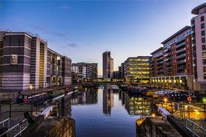 Dusk view of Leeds city centre canal, with modern waterfront buildings reflecting on the calm water, and moored boats.