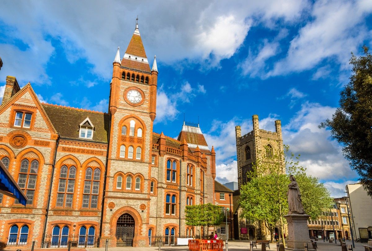Historic Reading Town Hall and clock tower, alongside St Laurence Church and Queen Victoria statue, under a bright blue sky in Reading, UK.